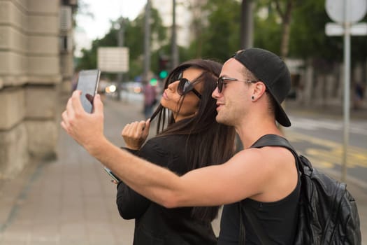 Two cheerful friends taking photos of themselves on smart phone, urban city outdoor scene, selective focus