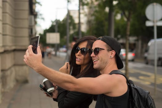 Cheerful friends taking photos of themselves on smart phone, urban city outdoor scene, selective focus