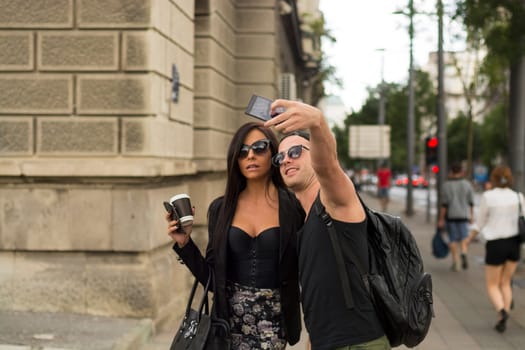 Cheerful friends taking photos of themselves on smart phone, urban city outdoor scene, selective focus