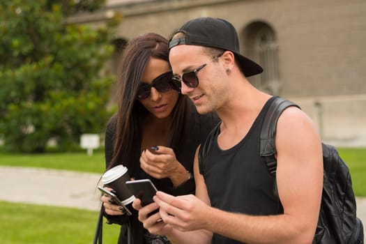 Two cheerful friends taking photos of themselves on smart phone, urban city outdoor scene, selective focus