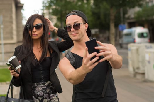 Cheerful friends taking photos of themselves on smart phone, urban city outdoor scene, selective focus