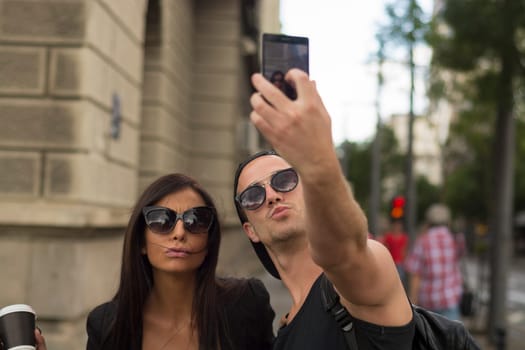 Young cheerful friends taking photos of themselves on smart phone, urban city outdoor scene, selective focus