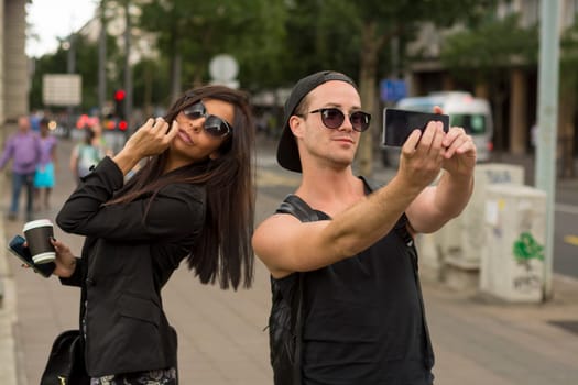 Cheerful friends taking photos of themselves on smart phone, urban city outdoor scene, selective focus