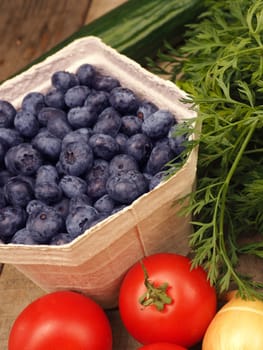 Freh fruits and vegetables, blueberries with tomatoes, carrots and onions on a rustic table