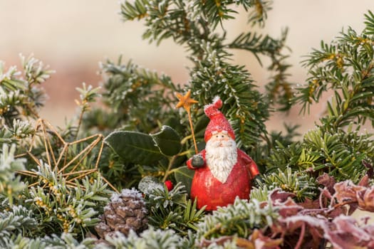 Christmas red St. Nicholas figure sits between fir branches in the frost