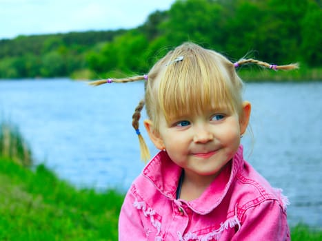 pretty fashionable smiling baby girl with nice plaits near the river