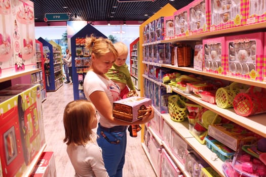 mother with her little daughters choose a doll in a toy shop