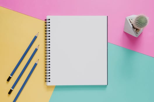 Office workplace minimal concept. Blank notebook, pencil, cactus on yellow, pink and green turquoise background. Top view with copy space, flat lay. Pastel color filter.