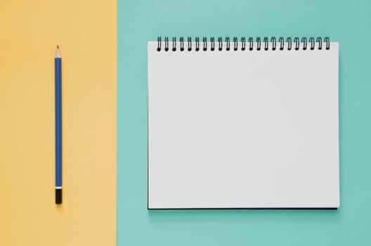 Office workplace minimal concept. Blank notebook, pencil on yellow and green turquoise background. Top view with copy space, flat lay. Pastel color filter.