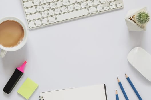 Office workplace concept. Computer keyboard with cup of coffee, blank notebook, note pad, computer mouse, cactus, marker color pen on white desk. Top view with copy space, flat lay.