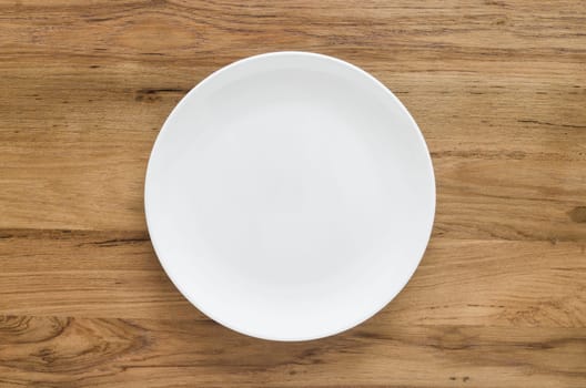 Empty white plate on wooden background. Top view with copy space. Flat lay.