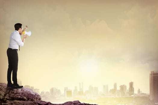 Asian business man standing on the top of mountain, screaming using megaphone