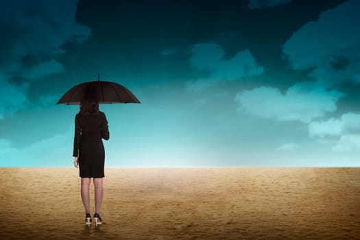 Business person holding umbrella standing on the desert