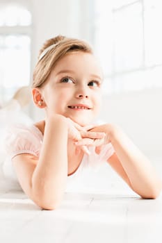 The little balerina in white tutu in class at the ballet school lying on the wooden floor