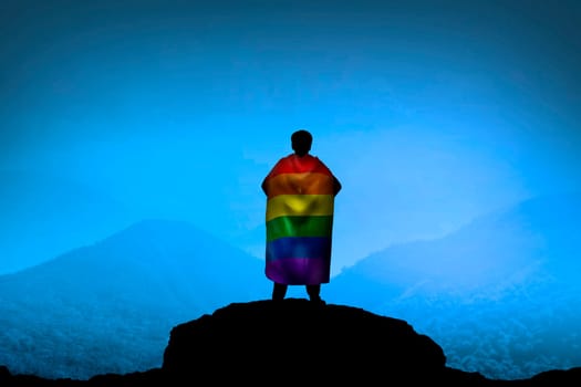 Silhouette of man looking at the mountain wearing LGBT flag as cape