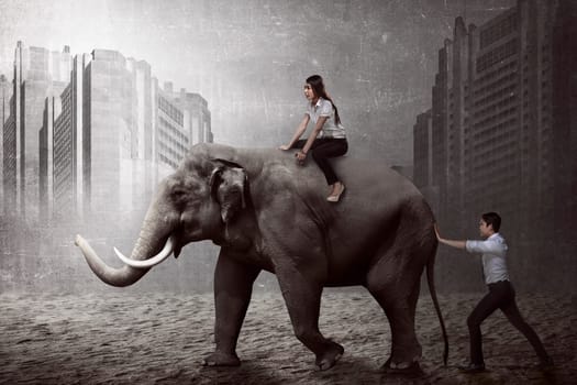 Asian business man push elephant while his friend sit on it back