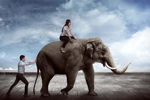 Asian business man push elephant while his friend sit on it back