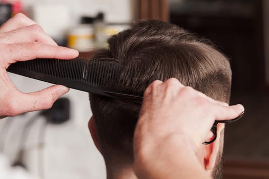The hands of barber making haircut to attractive man in barbershop
