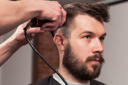 The hands of barber making haircut to attractive man in barbershop