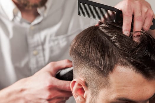 The hands of barber making haircut to attractive man in barbershop