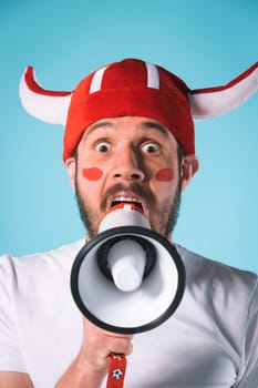 The football fan with megaphone over blue. The young man looking at camera with different emotions on face