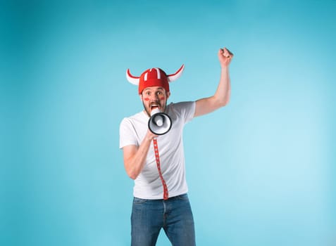 The football fan with megaphone over blue. The young man looking at camera with different emotions on face