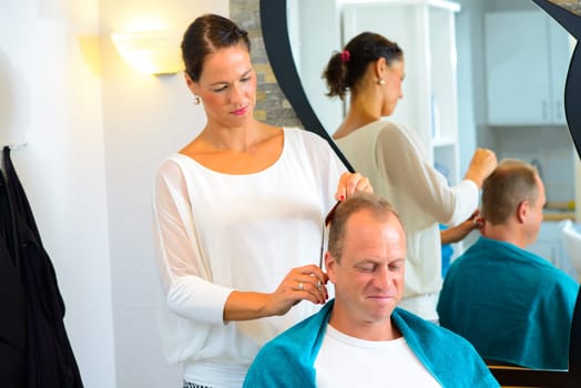 female hairdresser cutting hair of man in her shop