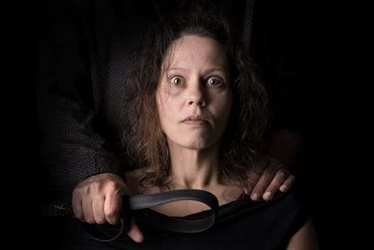 Abused woman victim of domestic violence, with husband hand holding a belt as a weapon.