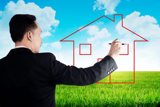 Business man drawing house on the meadow with blue sky background