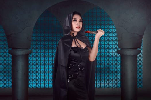 Young beautiful asian witch holding bloody knife on the old building