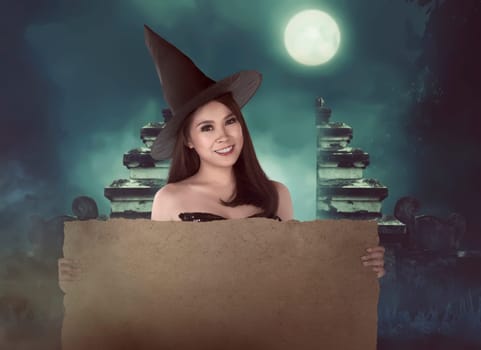 Halloween asian witch with hat holding blank paper in the night time