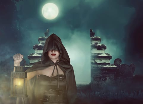 Young asian witch woman in black corset and cloak hooded with lantern in darkness