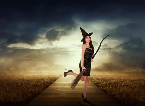 Beautiful asian witch woman with black hat holding broom on the meadow