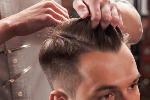 The hands of barber making haircut to attractive man in barbershop