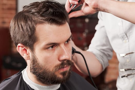 The hands of barber making haircut to attractive man in barbershop