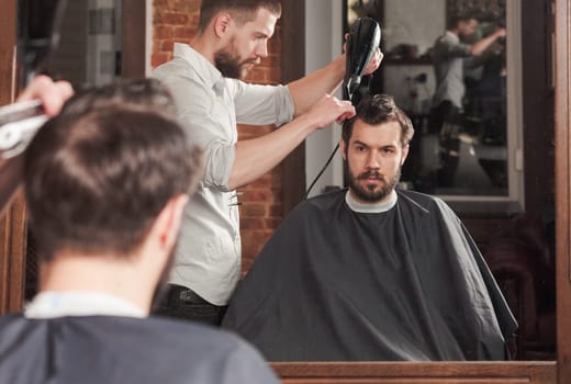 Young handsome barber making haircut of attractive bearded man in barbershop