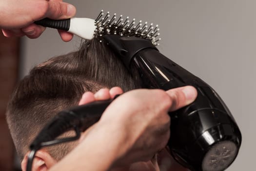 The hands of barber making haircut to attractive man in barbershop
