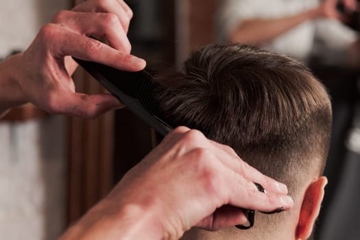 The hands of barber making haircut to attractive man in barbershop