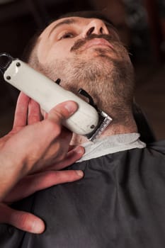 Hipster client visiting barber shop. The hands of young barber making the cut of beard