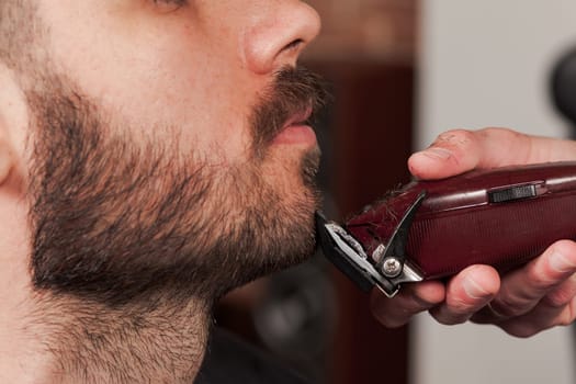 Hipster client visiting barber shop. The hands of young barber making the cut of beard