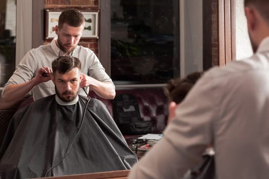 Young handsome barber making haircut of attractive bearded man in barbershop