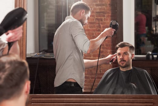 Young handsome barber making haircut of attractive bearded man in barbershop