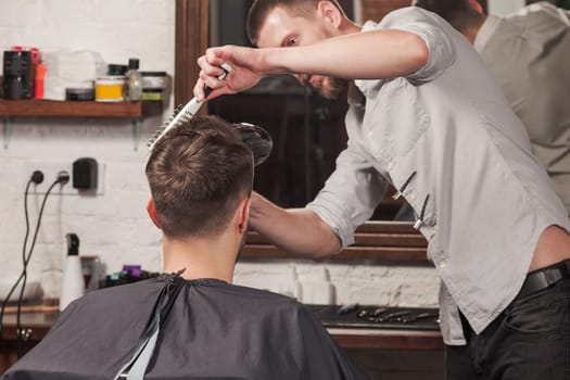 Young handsome barber making haircut of attractive bearded man in barbershop