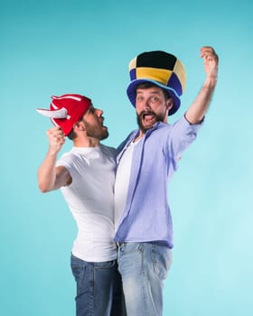 Two excited male friends celebrate watching sports on television over blue studio