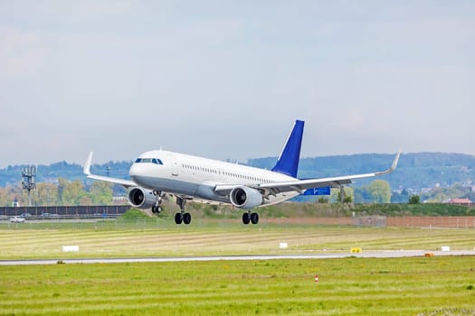 Airplane with blue tail fin on landing approach at airport - runway and green meadow in front
