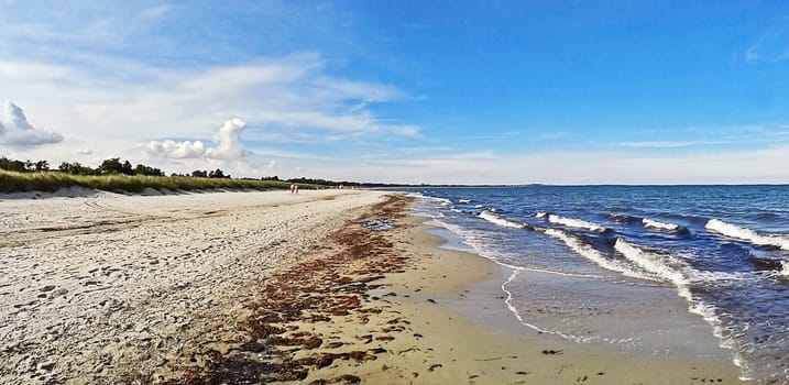 Beach in Marielyst, denmark with ocean waves of baltic sea and blue sky - panorama view
