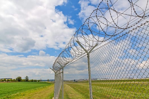 fence with barbed wire, green landscape and blue sky with clouds