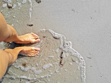 man standing with barefoot feet in water at beach