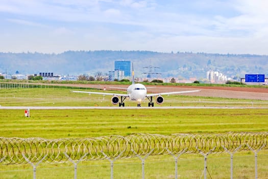 Airplane at ground on its way to runway before takeoff - green meadow with fence in front