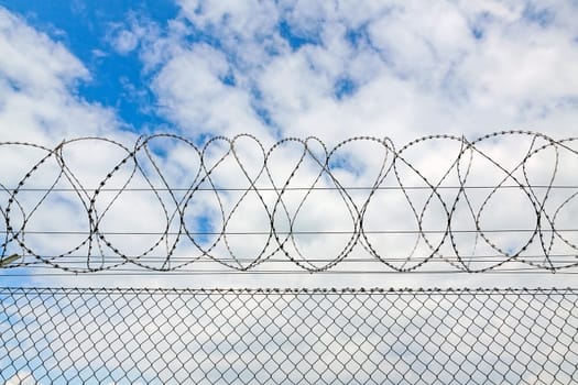 fence with barbed wire against blue sky with clouds